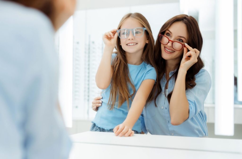 A parent and their child looking in the mirror at their optometrist's office, smiling and trying on a stylish new pair of glasses.