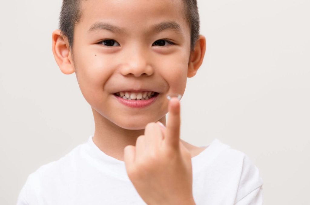 A child smiling while holding up a myopia control contact lens on the tip of their index finger.